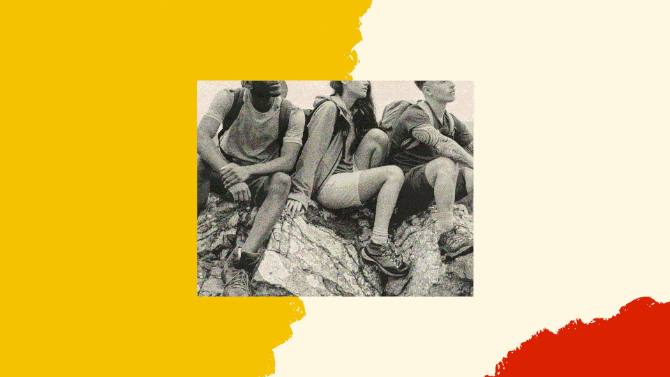 A black-and-white photo shows three hikers sitting on a mountain with backpacks on. They are looking out to the horizon.