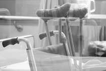 Black-and-white photo of crutches and a wheelchair in what seems to be a hospital