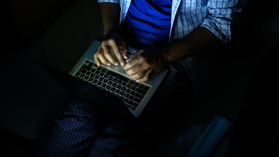A person typing on a laptop in the dark