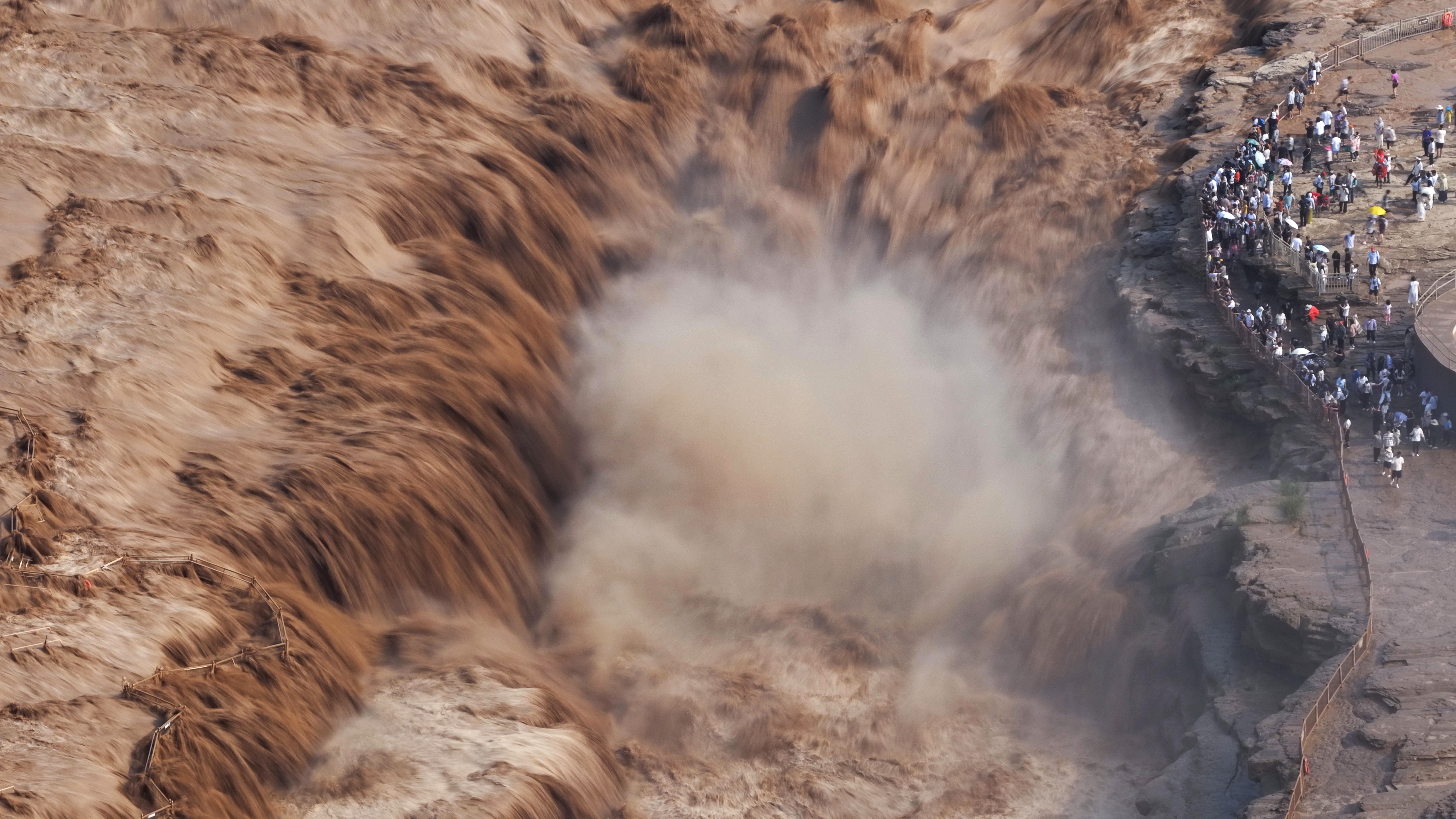 Rushing water cascades down a waterfall as a group of people watch from a nearby overlook.