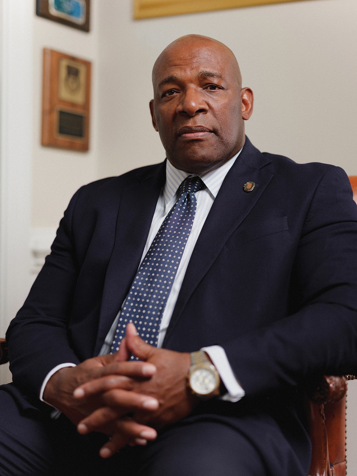 photo of bald Black man in suit and tie sitting with hands clasped