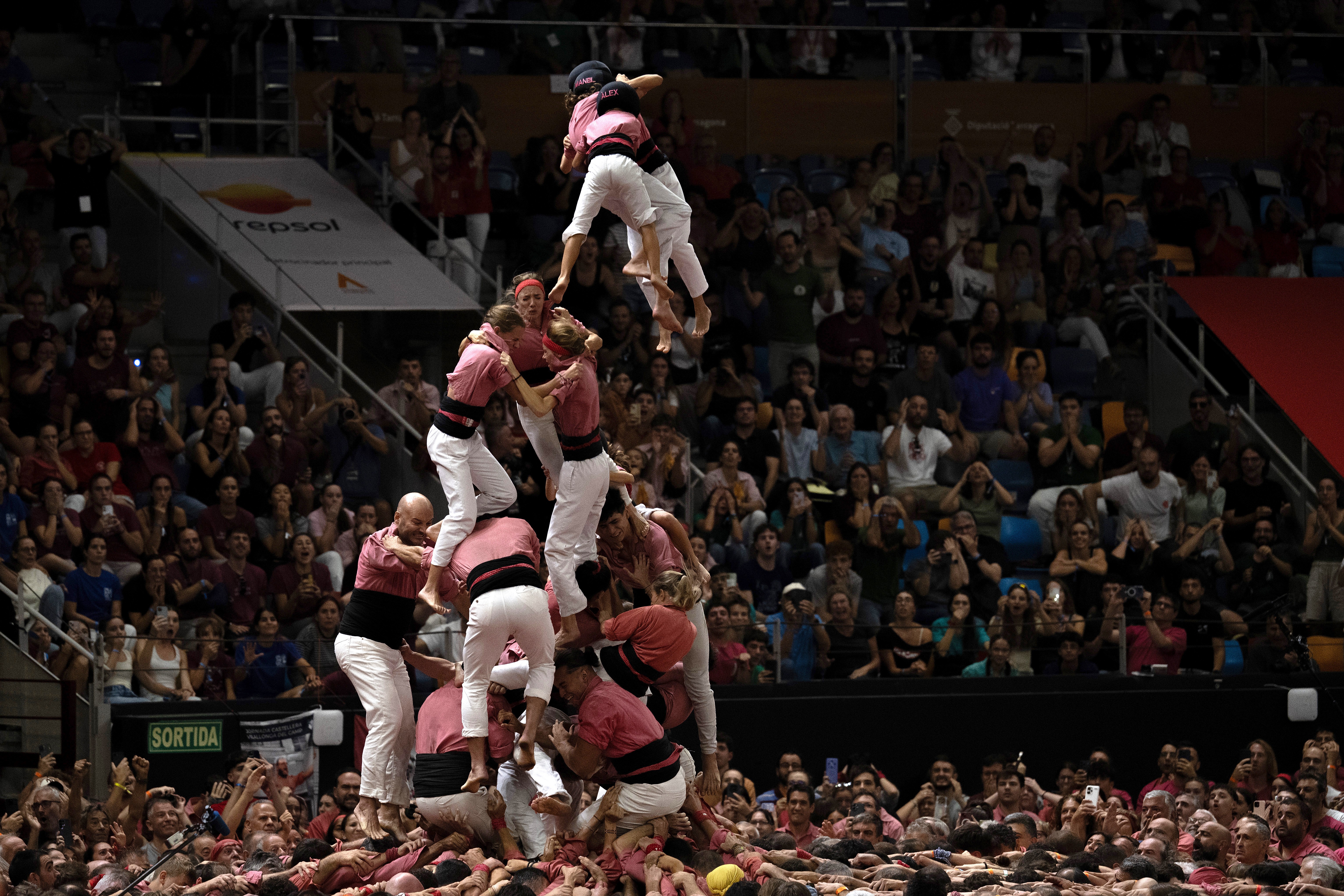 A partially-formed human tower collapses, with people falling toward their gathered team below.