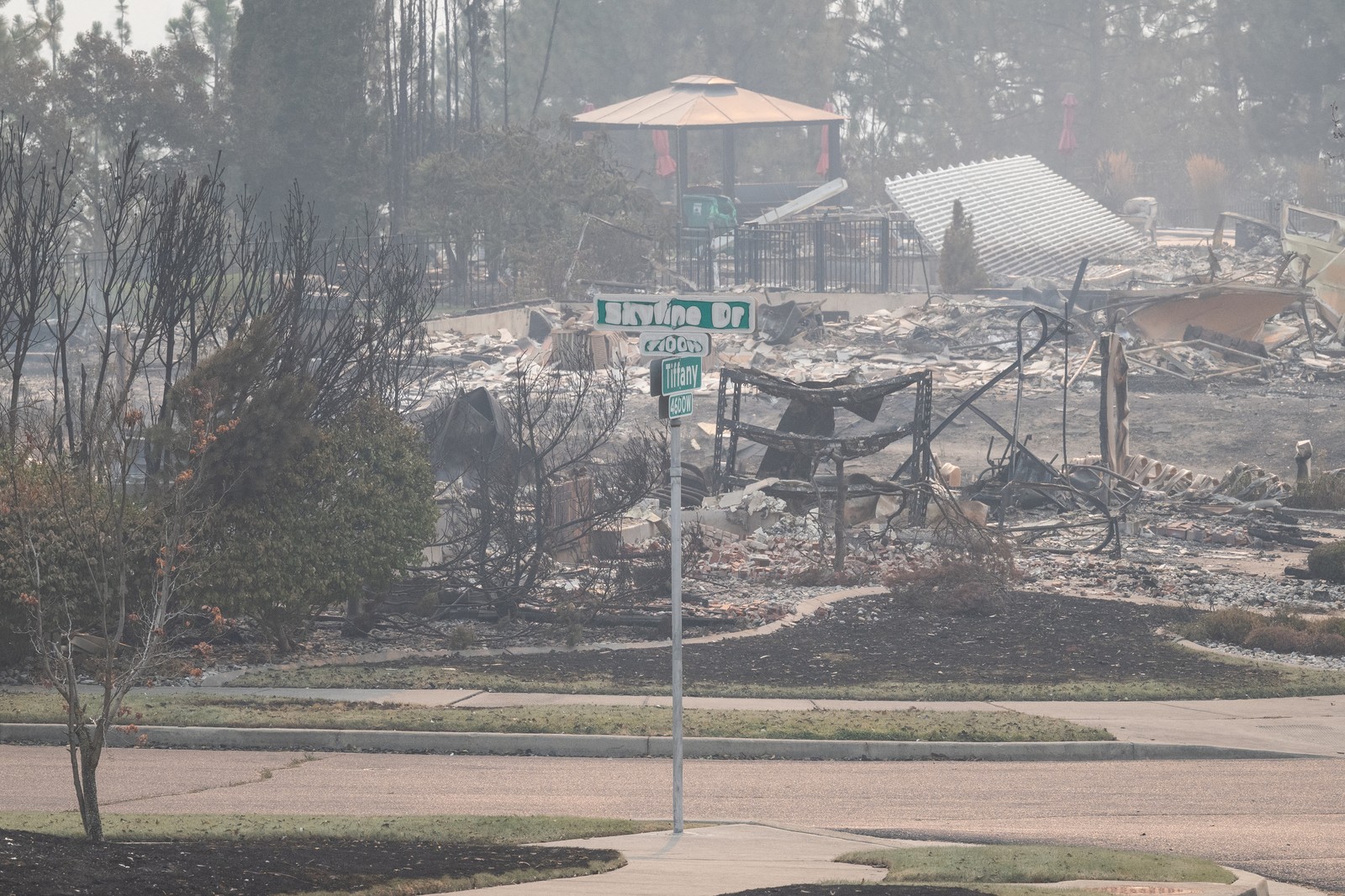 A partially-melted street sign sits in front of burned houses.