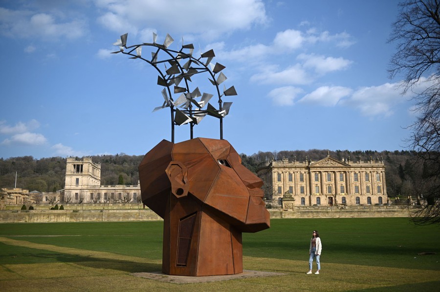 A person looks at a metal sculpture shaped like a large head with shapes suggesting flying books emerging from the top.