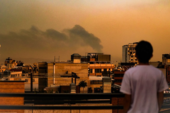 A boy looks out over Tehran as smoke fills the air after an airstrike from Israel