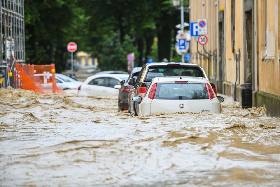 Several cars are caught in floodwater flowing down a street.