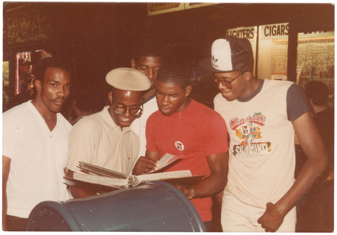 photo of 5 people in front of lit storefront looking at large album's pages at night