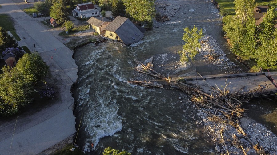 An aerial view of a flooding river that has destroyed parts of a road, bridge, and house.