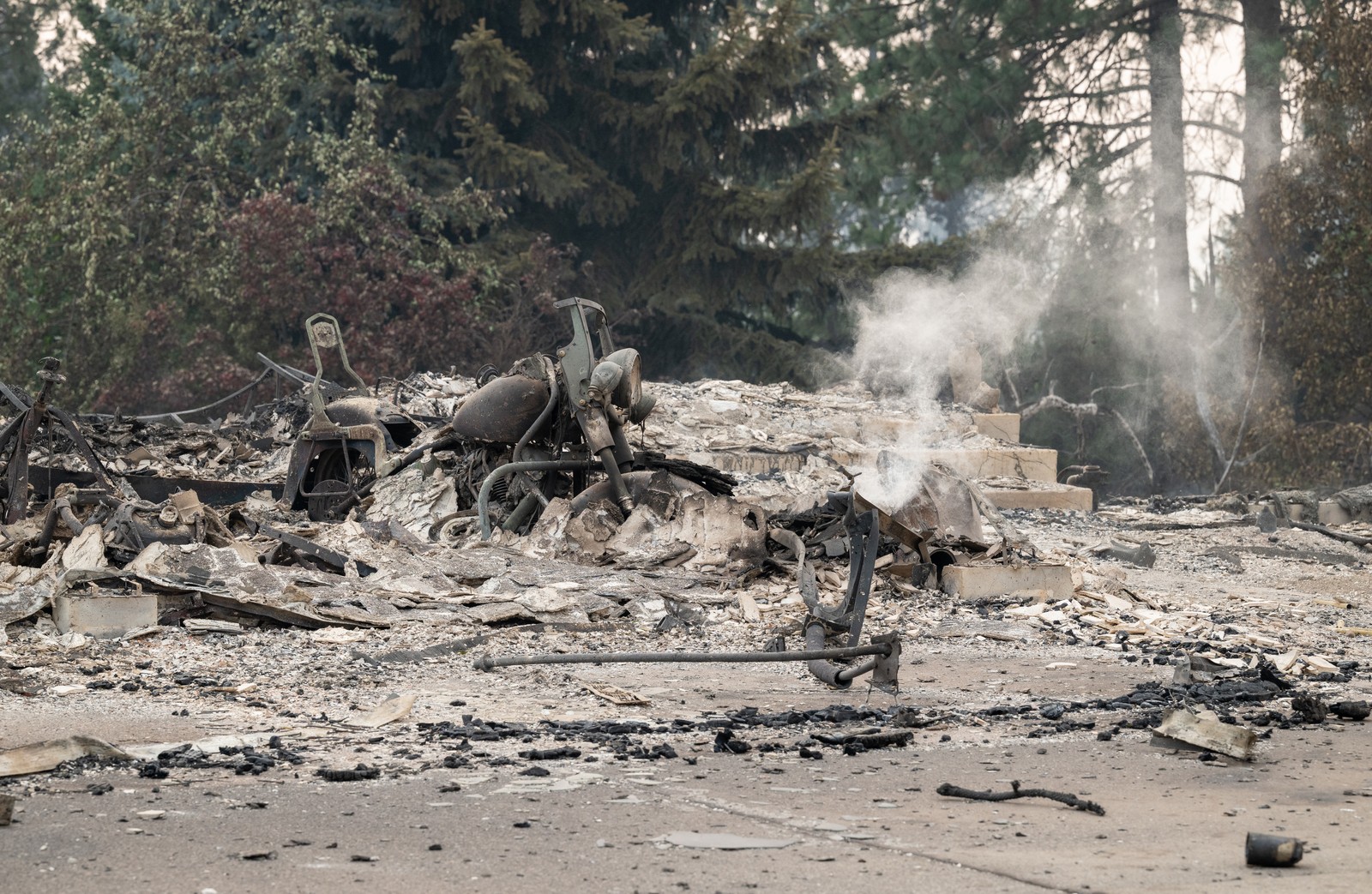 A burned motorcycle sits in the ashes of a burned-out home.