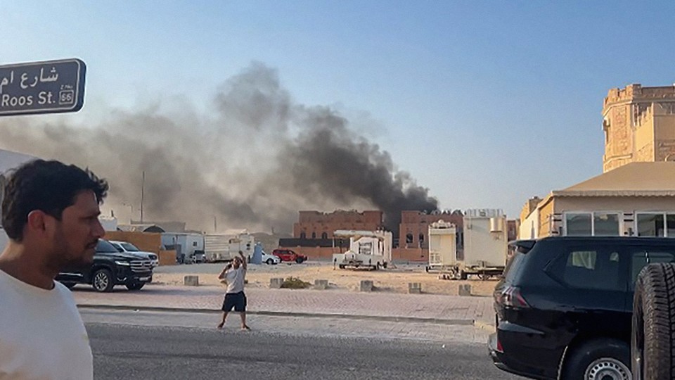 Color photograph of two men in the street in Doha, with black smoke rising in the background.