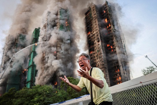A man reacts emotionally while standing outside a burning complex of tall residential buildings.