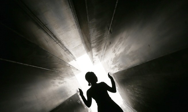 A silhouetted figure walking through a dark, narrow tunnel toward light.