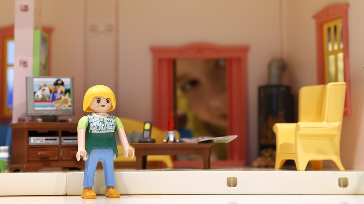 A Playmobil doll sits in her tiny, plastic living room.
