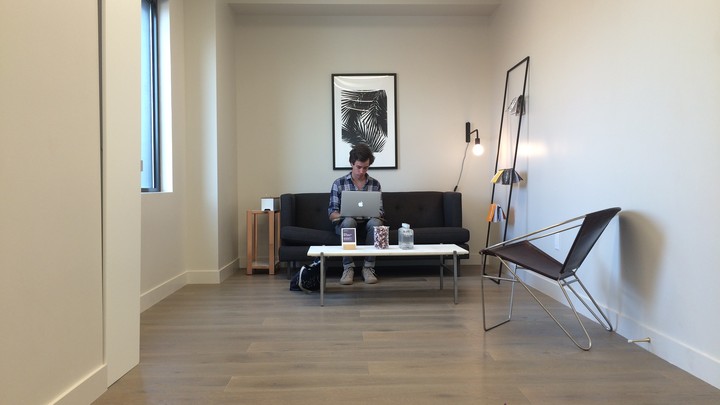 The author sits on a couch at his laptop in a Breather room.