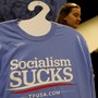 A T-shirt on a hanger reads "Socialism Sucks"; two young women stand behind it.