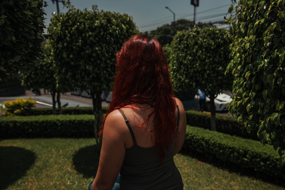 a red-haired woman facing away, with trees in the background