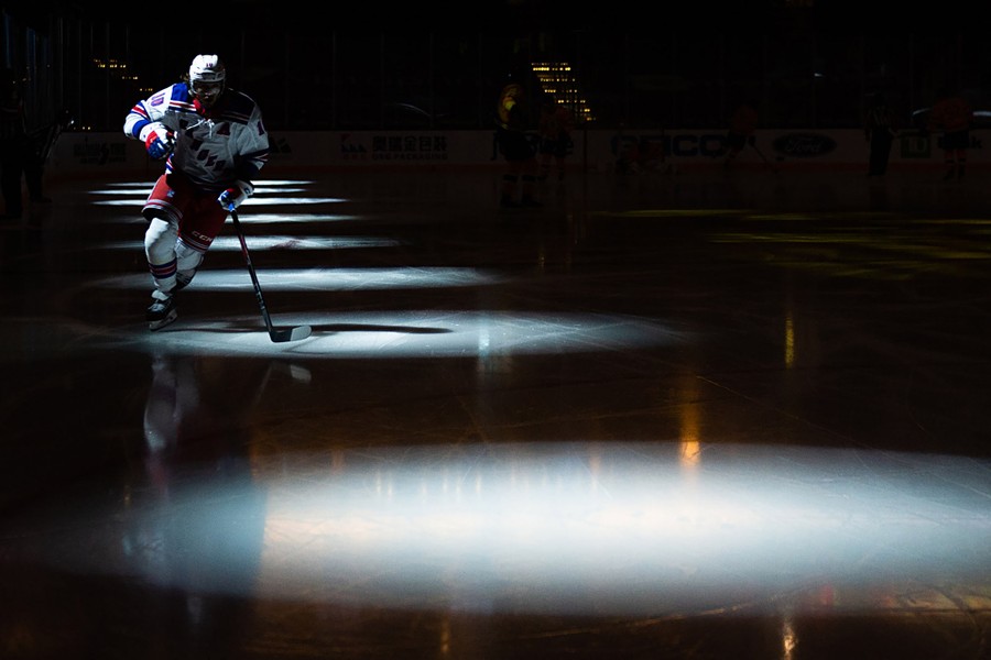 A hockey player skates through spotlights on a dark rink.