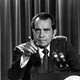 Black-and-white photo of Richard Nixon standing at a lectern with two microphones, facing the camera and pointing his finger at something or someone in the near distance