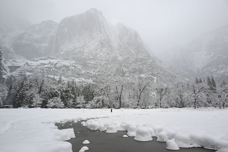 Mountains, a forest, a field, and a stream are seen, all covered in snow.