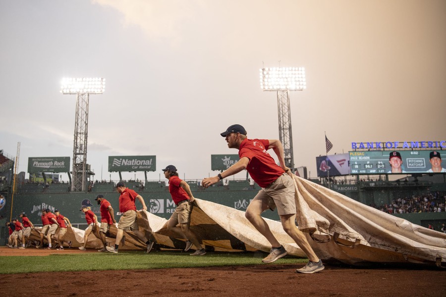 About a dozen ground-crew members run, pulling a huge tarp across a baseball field.
