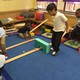 A group of pre-school students play on a blue carpet with wooden ramps and balls.