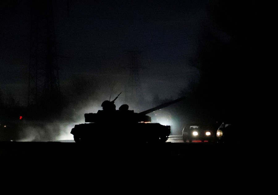 A dark silhouette of a tank is seen on a street at night.