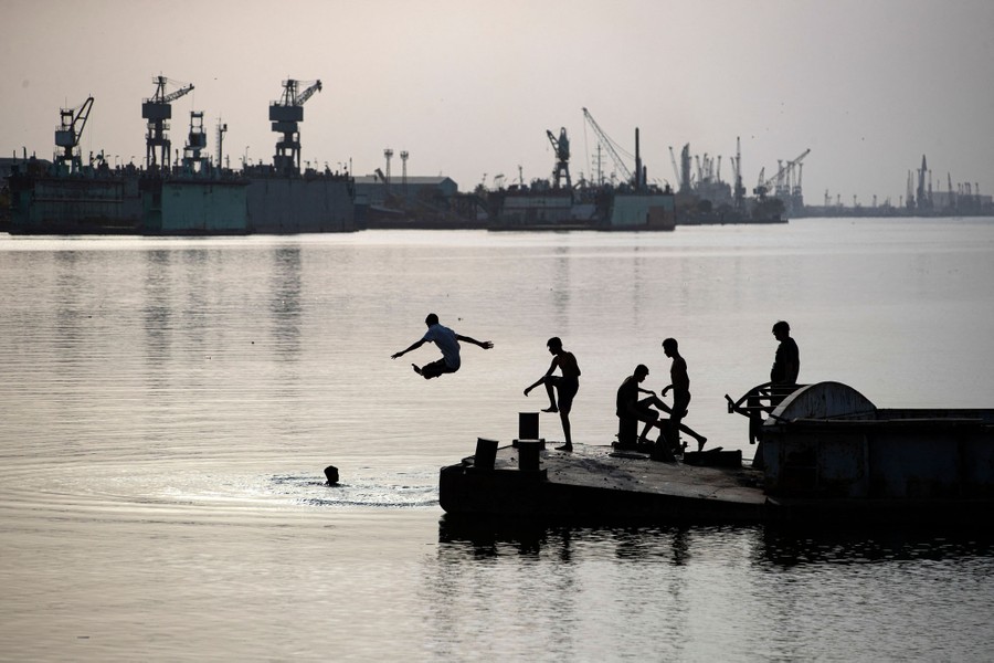 Several young people climb on and leap from a dock into a broad river.