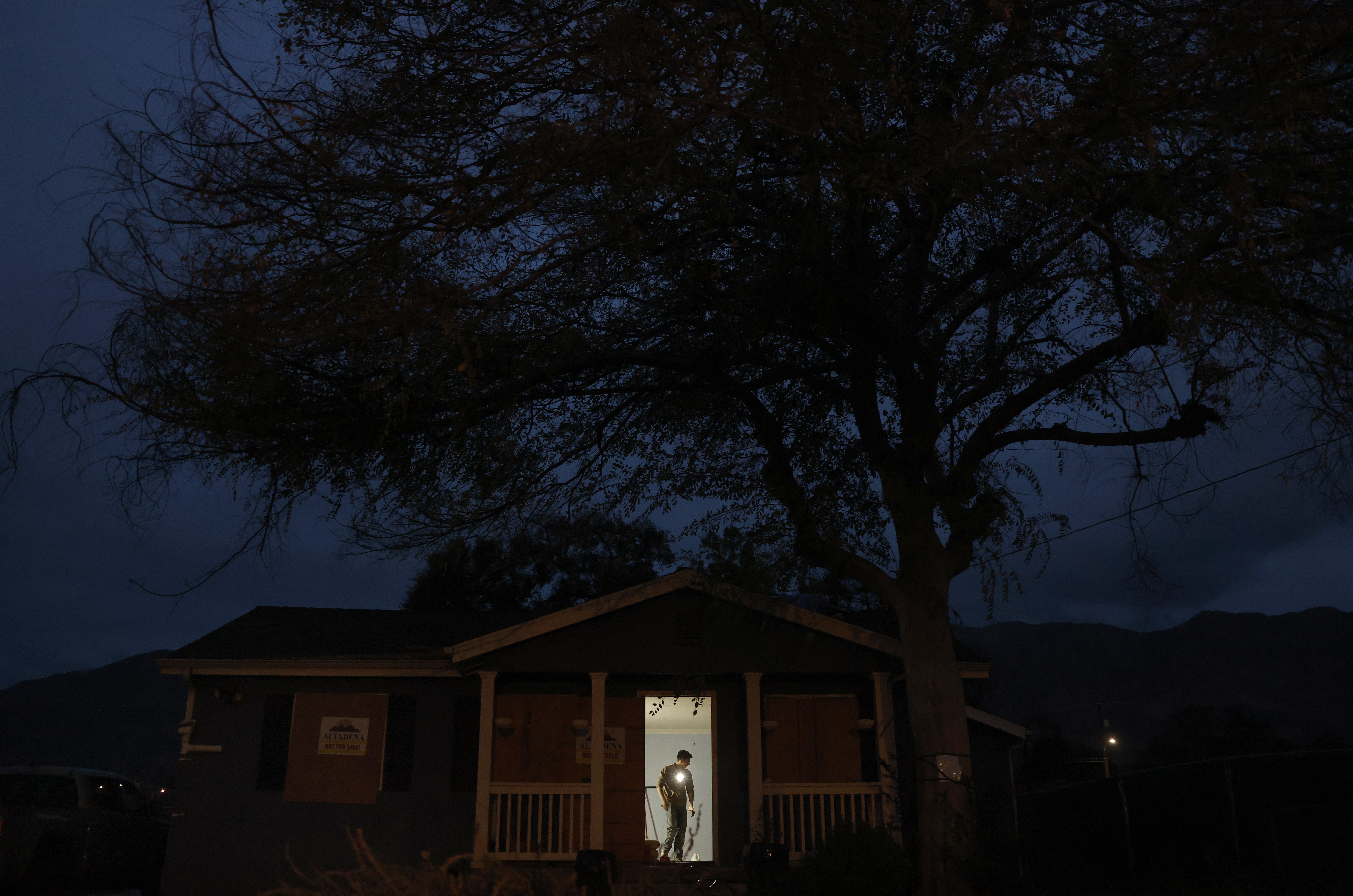 A person is seen working inside a house, viewed from outside, through an open door, at night.