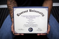 A man with tattoos on his arm holds a diploma.