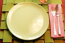 A place setting for one: A light green plate on a green woven placemat with a knife and fork sitting on a plaid napkin. A half-full glass of wine sits by the plate.