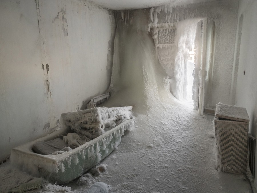 Huge volumes of ice intrude into a bathroom, entering from an open door, the walls and ceiling.