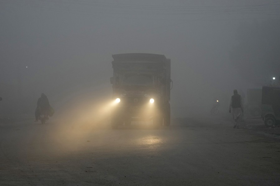 People walk and drive on a road enveloped in smog.