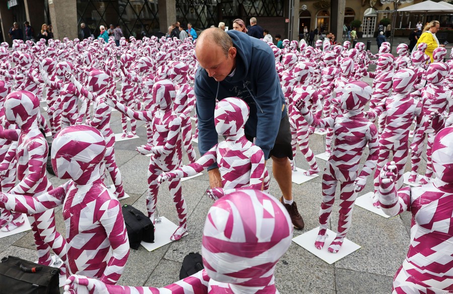 A person adjusts one of hundreds of child-sized mannequins, covered in colored tape, arranged in a city square.