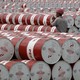 A worker walks between stacks of red and white oil barrels.