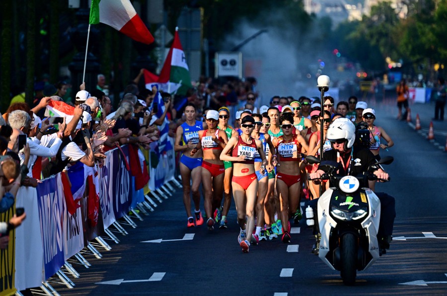 Competitors in a walking race pass by a crowd.