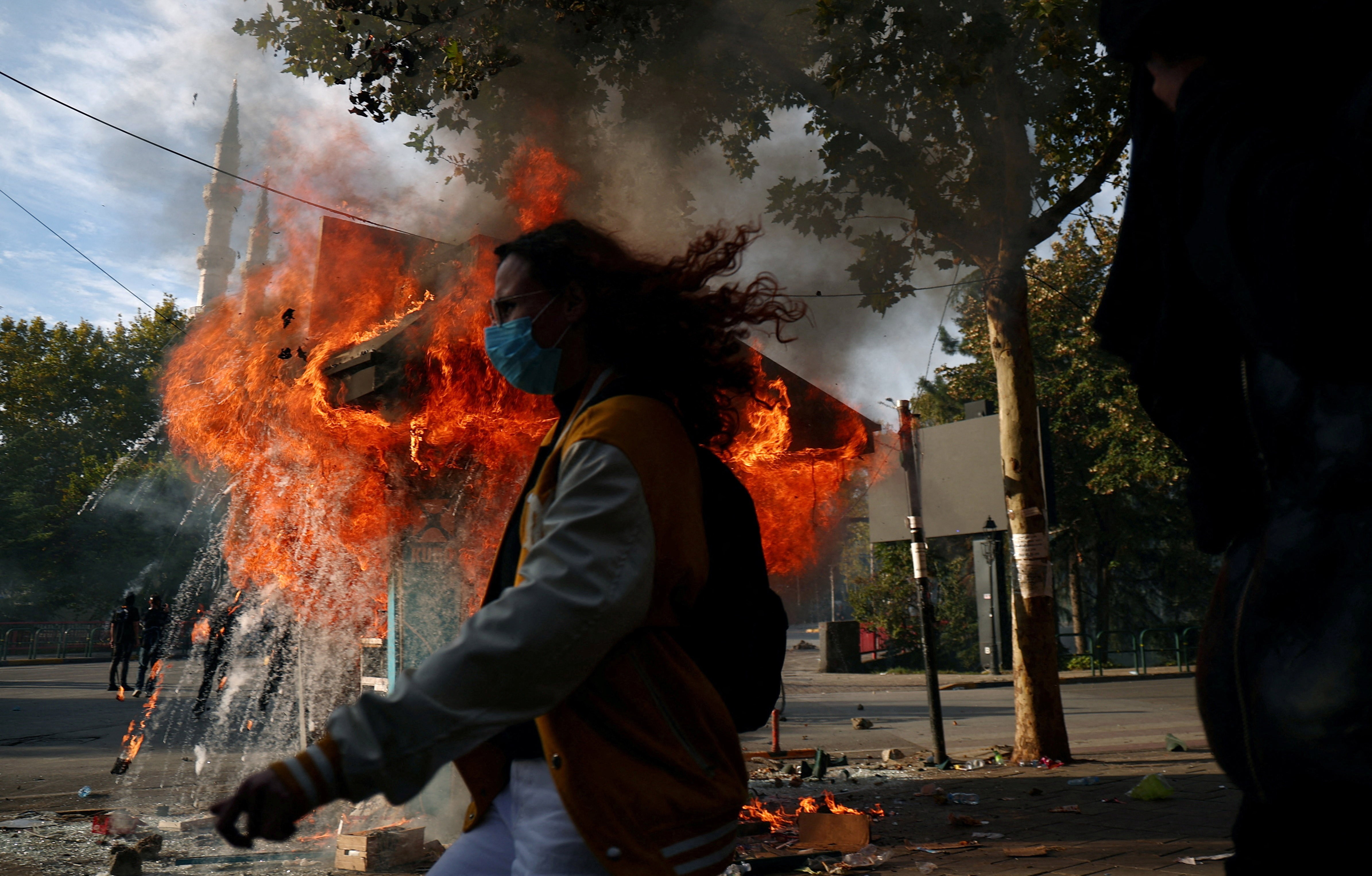 A person walks past a burning kiosk during a protest.