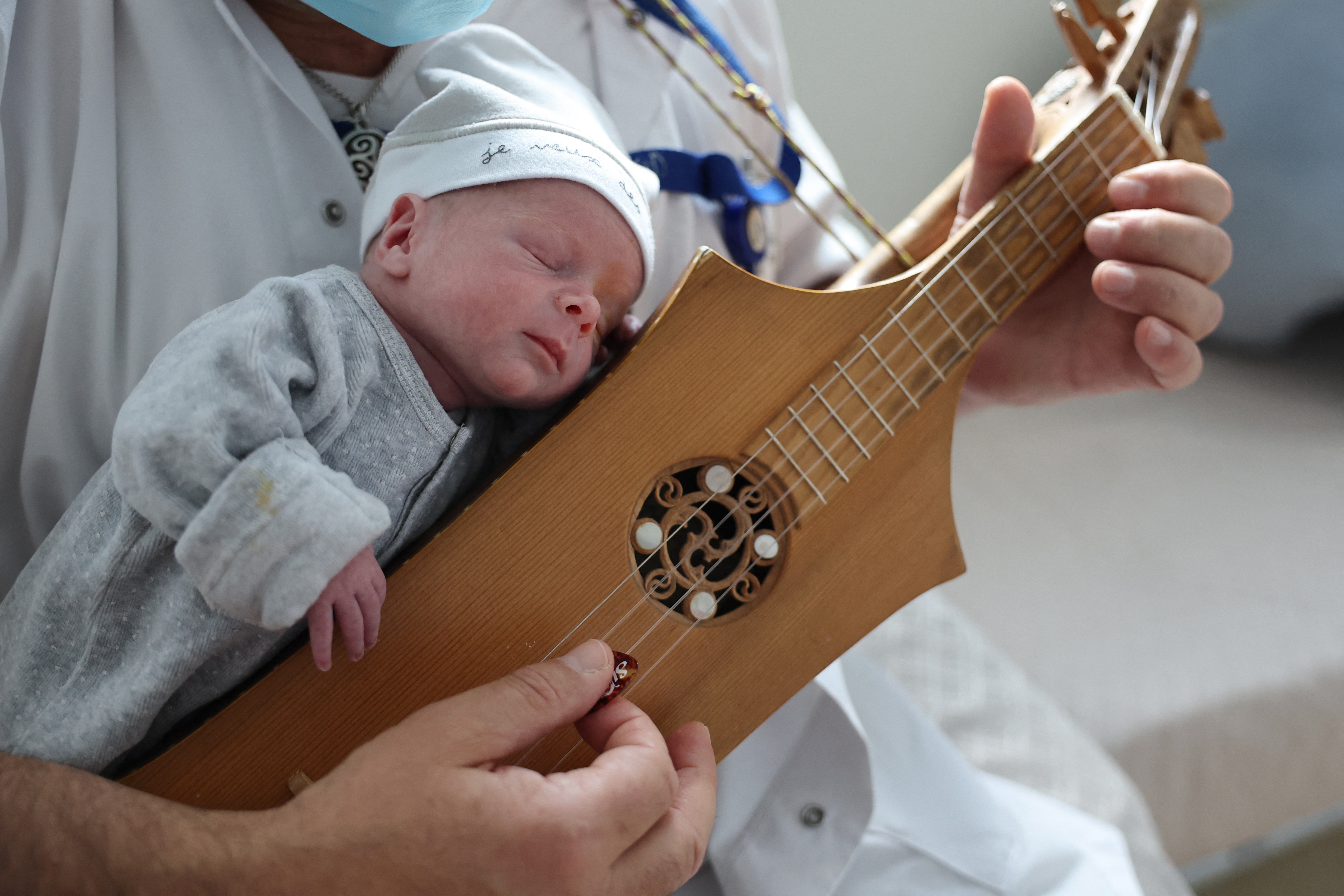 A newborn child rests on the chest of a person playing a traditional stringed instrument.
