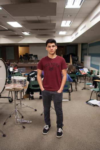 A student stands next to a set of drums. 