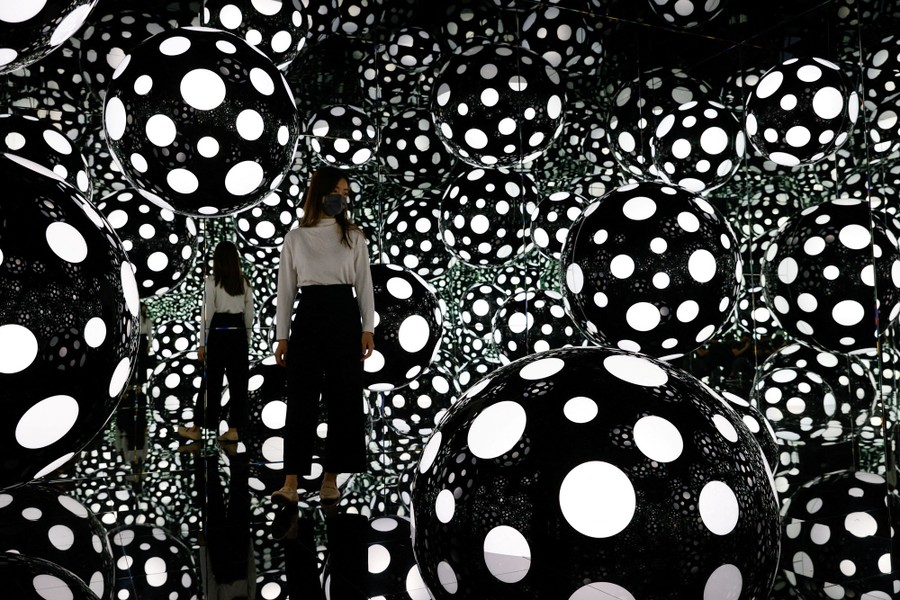 A person stands among illuminated spheres in a mirror-walled room.