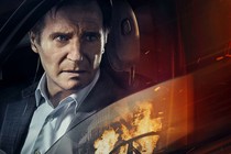 Liam Neeson in a car, looking at a fire outside