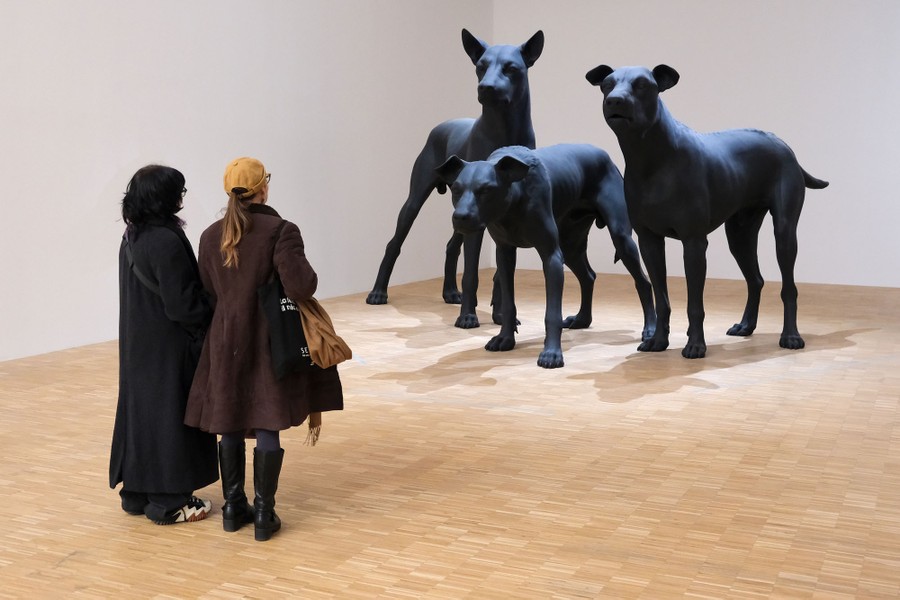 Two people look toward three large dog sculptures.