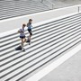 A man and woman jog down cement stairs together.