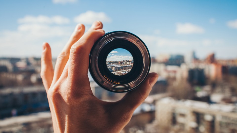 A view of a city through a camera lens held up by a hand