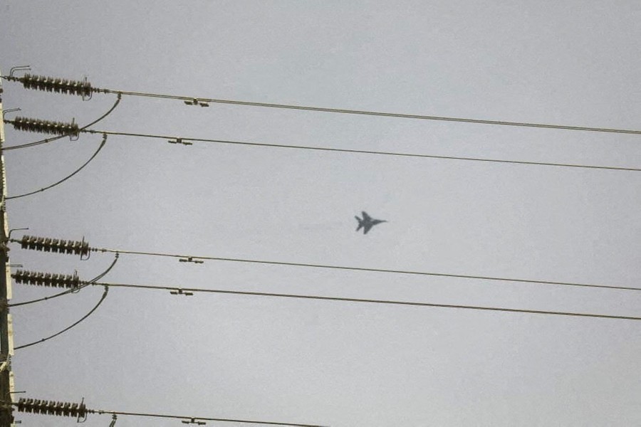 A military jet fighter flies, seen through a set of power lines.