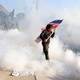 A person carries an American flag as they walk through a cloud of tear gas at a protest outside of an ICE facility.