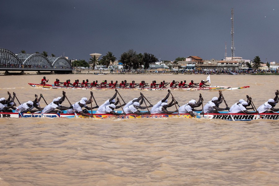 Two teams of rowers in very long boats race on a broad river.
