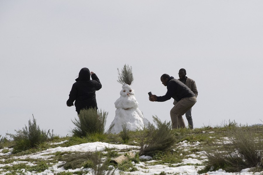 Several people take photos of a snowman.