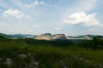a field of grass and a rock formation in the distance, under a wide blue sky