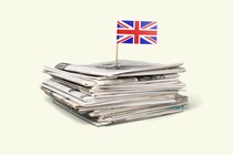 A pile of newspapers with a British flag planted on top