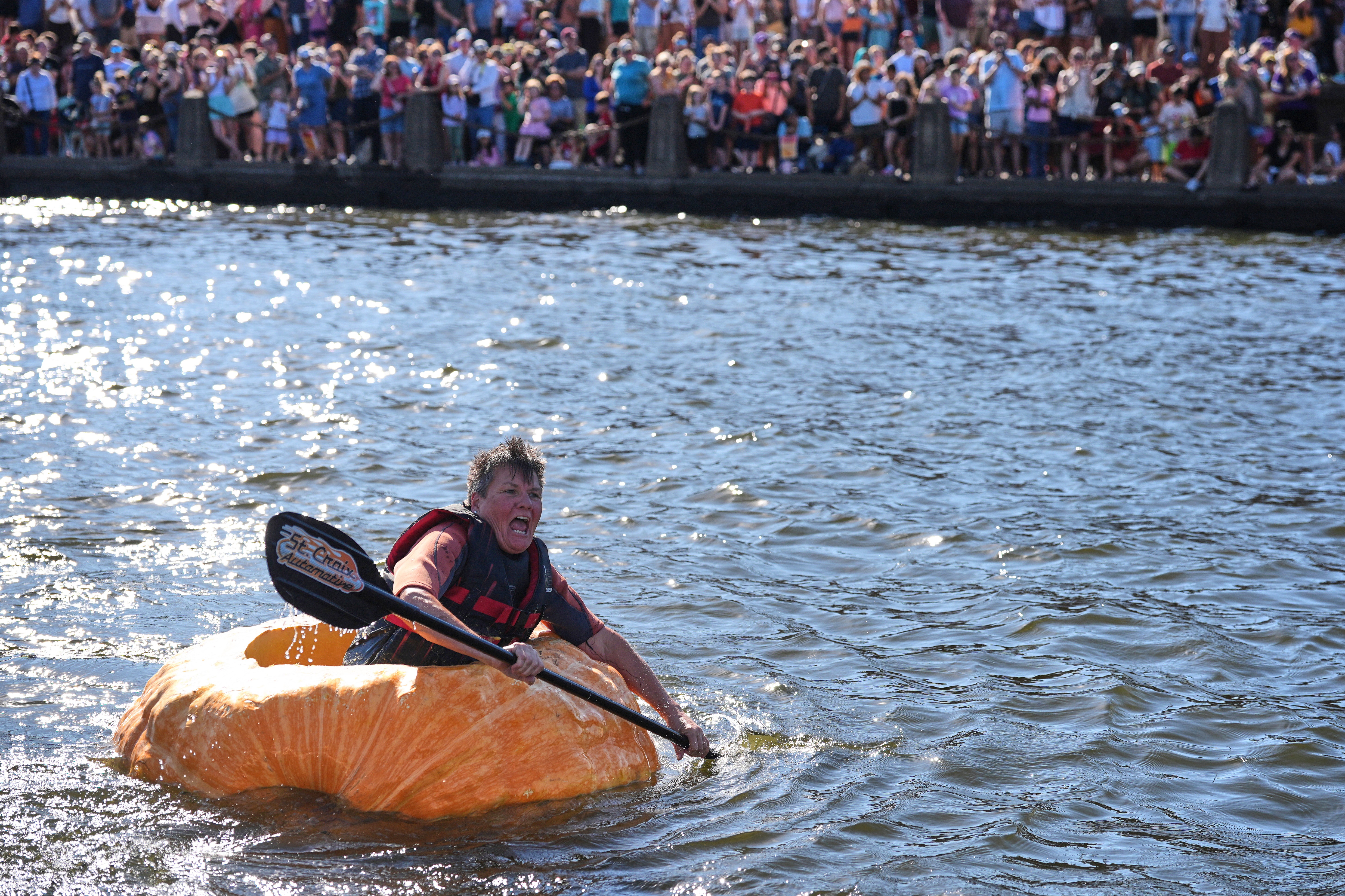 A person shows the effort on their face as they paddle a giant pumpkin to the finish line of a race.